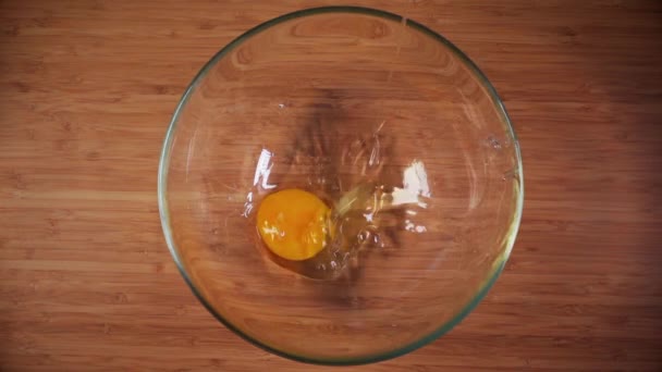 Top plan ingrediënten op een houten tafel. Rauwe eieren werden gebroken in een glazen kom. Dichtbij schot. Langzame beweging - Video