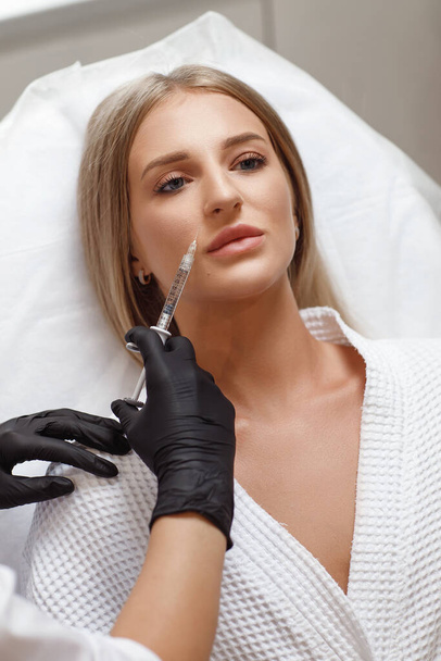 Powiększenie ust, korekta warg. Portret białej kobiety podczas operacji wypełniania zmarszczek na twarzy. - Zdjęcie, obraz