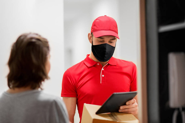 delivery man in mask with tablet pc and box - Foto, Bild