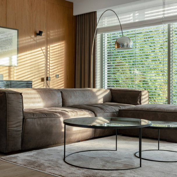 Elegant living room with big and comfortable couch, two modern coffee tables and silver lamp with big windows with garden view - Zdjęcie, obraz