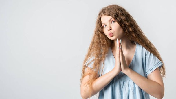 Please, help me. Emotive pleased European girl with curly long hair, keeps hands in praying gesture, beggs for giving good advice, dressed in casual t shirt. Isolated over white background. - Photo, Image