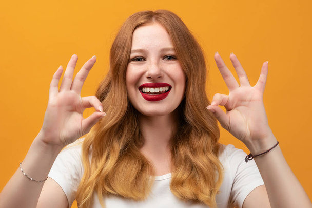 Happy girl with long wavy redhead, wearing white t-shirt Smiling and showing OK a two-handed gesture. I like that. Good job. Everything is great - Fotografie, Obrázek