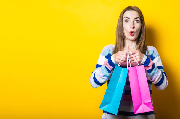 Young woman in sweater holds shopping bags with purchases on yellow background. - Foto, imagen