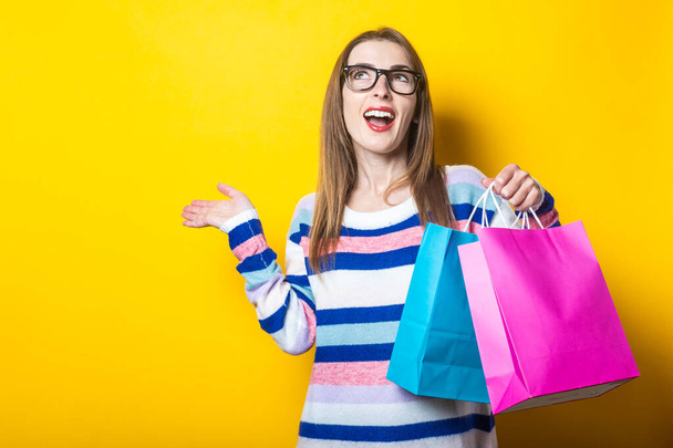 Young woman in sweater holds shopping bags with purchases on yellow background. - Φωτογραφία, εικόνα