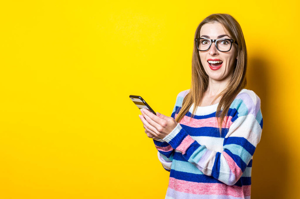 Young woman with a surprised face and holding a phone on a yellow background. Banner. - Photo, Image