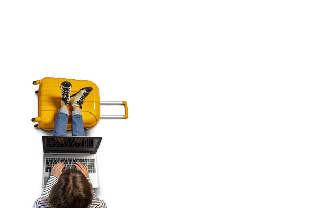 Giovane donna è seduta in aeroporto in attesa di un volo con i piedi su una valigia e lavorare su un computer portatile. Posa piatta, vista dall'alto. - Foto, immagini