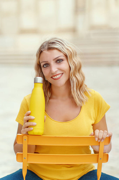 Νεαρή γυναίκα με κίτρινο t-shirt που κρατά κίτρινο επαναχρησιμοποιήσιμο μπουκάλι  - Φωτογραφία, εικόνα