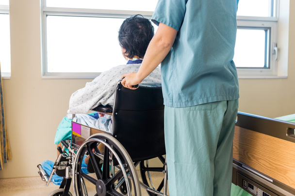 Nurse Holding Patient's Wheelchair's Handle By Window - 写真・画像