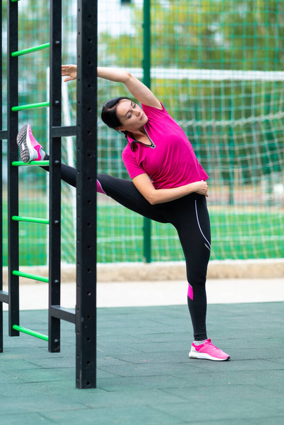 Fit muscular young woman doing a yoga side stretch with leg raised on a gym ladder outdoors at a sporting facility in a health and fitness concept - Photo, Image