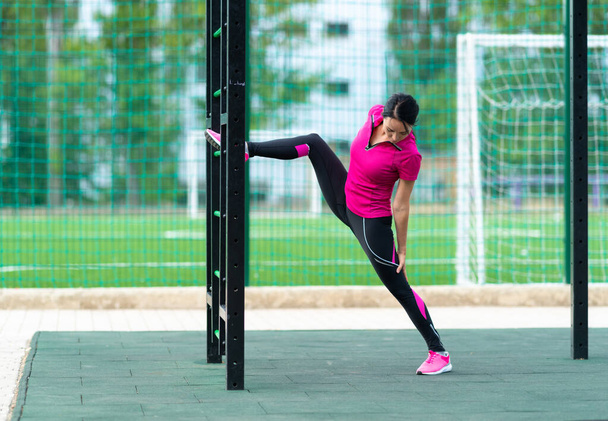 Young woman doing a back stretch or lunge to strengthen and tone her leg and thigh muscles at an outdoor gym in a health and fitness concept - Zdjęcie, obraz
