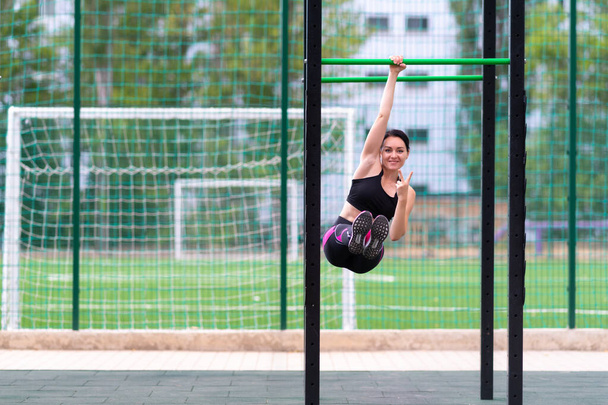 Young woman gesturing and smiling during a workout on parallel bars at an outdoor sports facility in a health and fitness concept - Fotografie, Obrázek