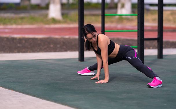 Fit sporty young woman doing the splits lowering herself down onto the ground at an outdoor gym in a health and fitness or active lifestyle concept with copyspace - Foto, imagen