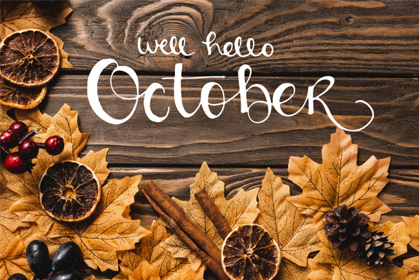Top view of autumnal decoration and foliage near well hello october lettering on wooden background - Фото, изображение