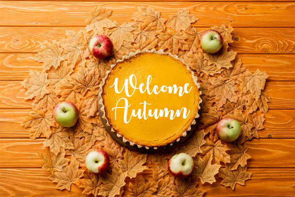 vista superior de pastel de calabaza de acción de gracias con manzanas en hojas cerca de la bienvenida con letras de otoño sobre fondo de madera - Foto, Imagen