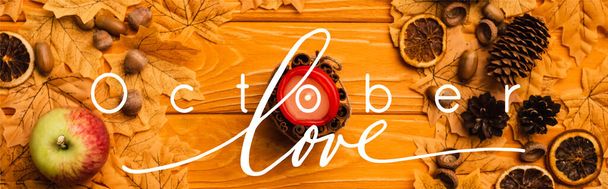 top view of burning candle with autumnal decoration near october love lettering on wooden background, panoramic crop - 写真・画像