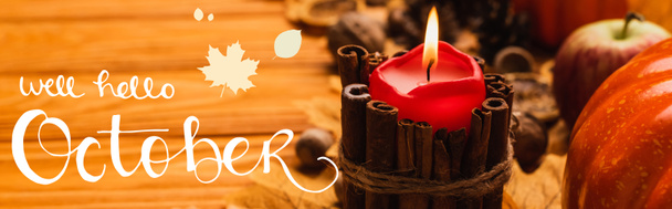 selektiver Brennpunkt brennender Kerze mit herbstlicher Dekoration in der Nähe des Brunnens Hallo Oktober Schriftzug auf Holzgrund, Panoramaaufnahme - Foto, Bild