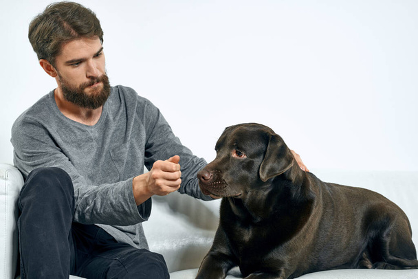 uomo con un cane nero su un divano bianco su uno sfondo leggero primo piano ritagliato vista animale domestico amico umano emozioni divertimento - Foto, immagini