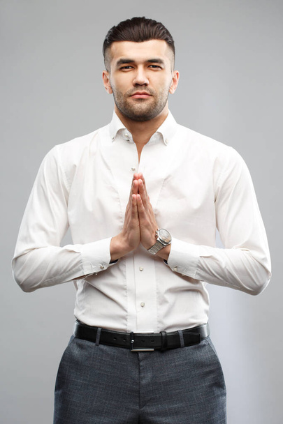 Handsome casual man standing folded hands in the pose of prayer  isolated on a gray background. - Photo, image