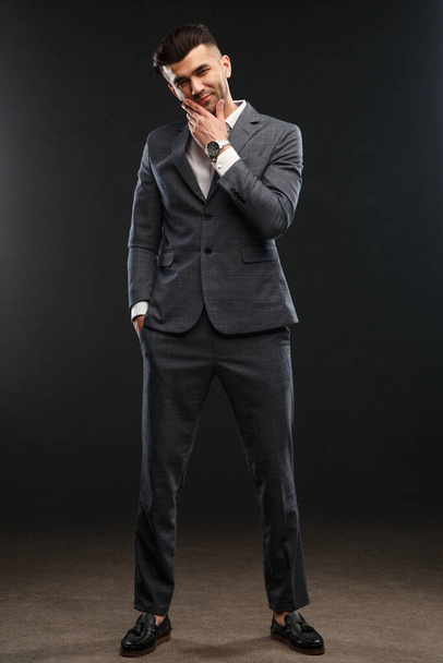 Egy elegáns férfi egy üzleti öltönyben teljes növekedésben áll, sötét háttérrel.. - Fotó, kép