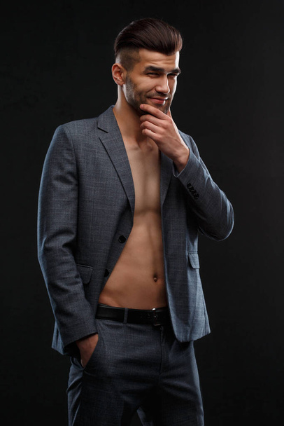Young sexy man in a jacket over his naked body against a dark background. - Fotó, kép