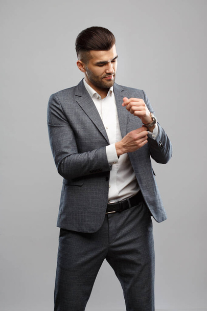 Young stylish man in elegant suit straightens wardrobe, isolated on gray background. - Foto, imagen
