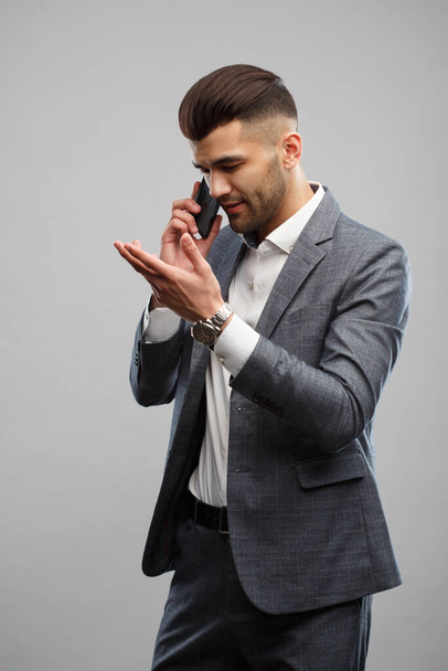 Stylish young man in an elegant suit talking on the phone gesturing with hands isolated on a gray background. - Fotó, kép