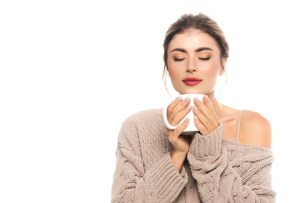 pleased woman in knitted sweater holding cup of warm beverage with closed eyes isolated on white - 写真・画像