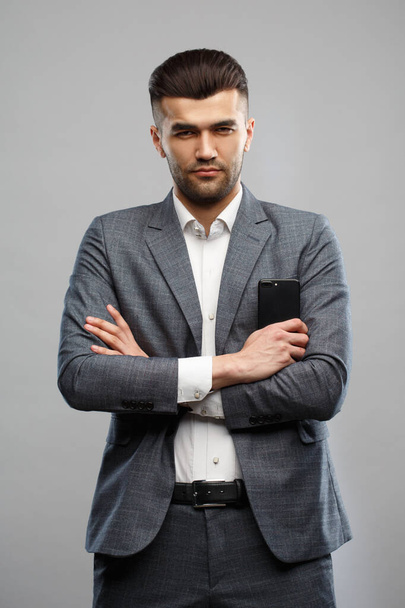 Young Asian man in a business suit holds a smartphone in his hand Isolated on a gray background. - Valokuva, kuva
