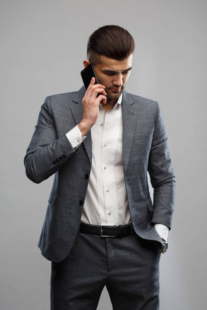 Young Asian man in a business suit talking on the phone Isolated on a gray background. - Фото, изображение