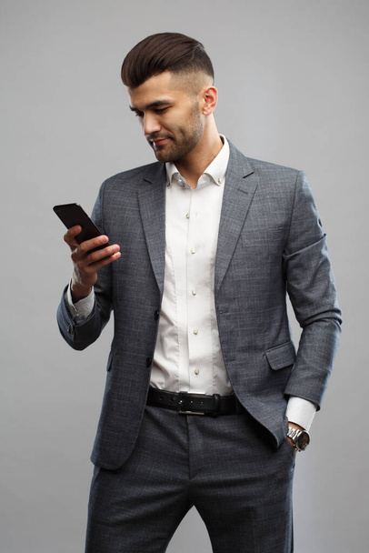 Young Asian man in a business suit holds a smartphone in his hand Isolated on a gray background. - Photo, image