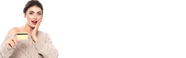 cultivo panorámico de mujer excitada en suéter de punto con tarjeta de crédito y rostro conmovedor aislado en blanco - Foto, Imagen