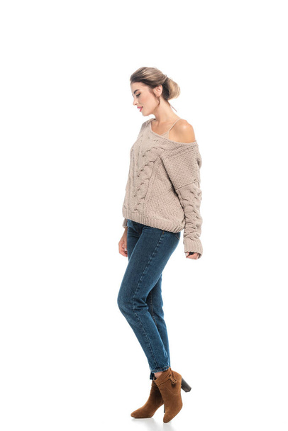 volledige weergave van modieuze vrouw in open werk trui en jeans poseren op wit - Foto, afbeelding