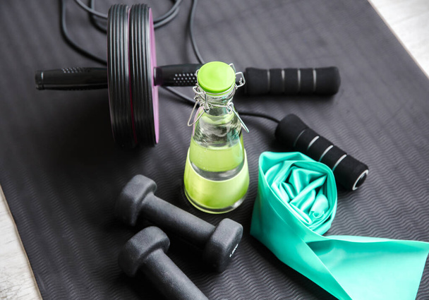 Selective focus on glass water bottle cap. Consuming fresh pure water during workout concept. Bottle on exercise mat with other training equipment. Keep hydrated. - Photo, Image