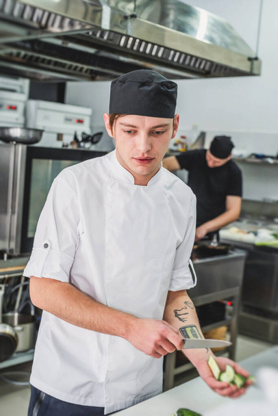 cook in white uniform working at the kitchen of the restaurant - Zdjęcie, obraz