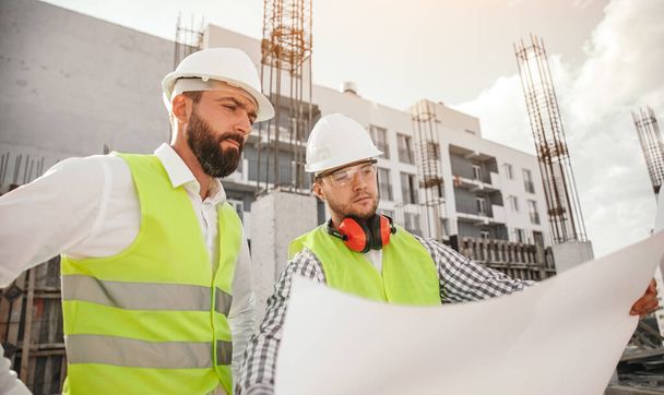 Male builders reading drafts on construction site - Fotografie, Obrázek