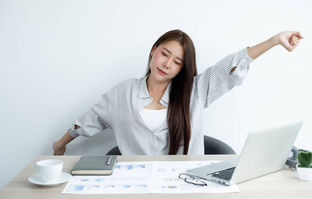 Le donne asiatiche sono stanche dal lavoro sul computer portatile si siede su una sedia che si estende per rilassarsi e rilassarsi mentre si lavora duramente in ufficio. - Foto, immagini