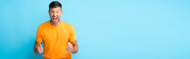 excited man with open mouth and clenched fists on blue, banner - Foto, Imagen