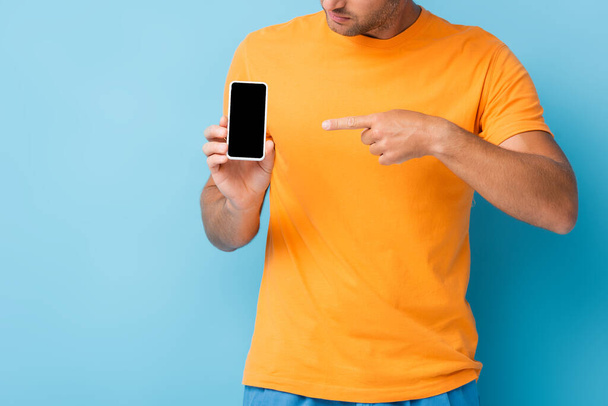 cropped view of man in t-shirt pointing with finger at smartphone with blank screen on blue - Фото, зображення