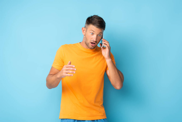 upset man man in t-shirt talking on smartphone on blue - Valokuva, kuva