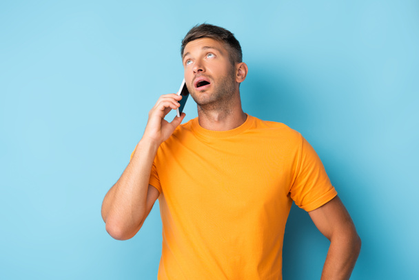 man in t-shirt aan het praten op smartphone en omhoog kijkend op blauw - Foto, afbeelding