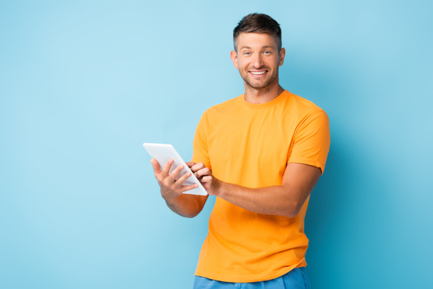 Mavi tişörtlü mutlu adam elinde dijital tablet tutuyor. - Fotoğraf, Görsel