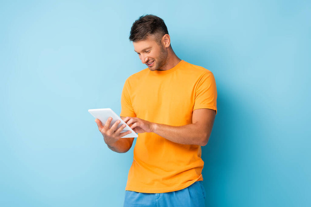 happy man in t-shirt using digital tablet on blue - Valokuva, kuva