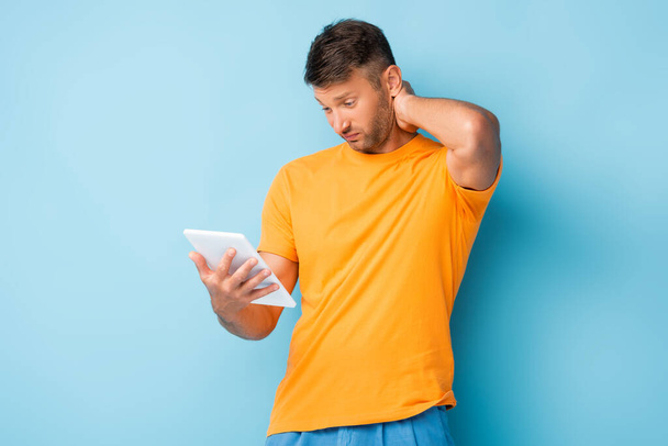 homem confuso em t-shirt usando tablet digital em azul - Foto, Imagem