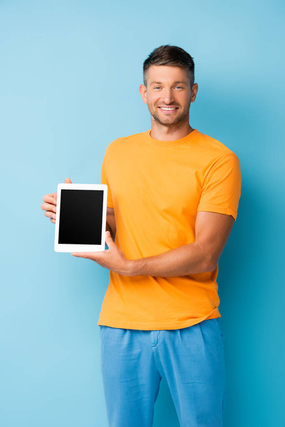 hombre complacido en camiseta sosteniendo tableta digital con pantalla en blanco en azul - Foto, imagen