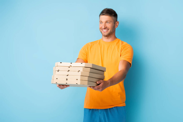 vrolijke man in t-shirt met kartonnen pizza dozen op blauw - Foto, afbeelding