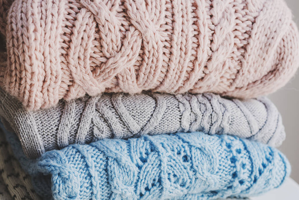Stapel van handgemaakte gebreide truien van lichtroze, grijs en blauwe kleur. Breigoed verzorgingsconcept. Warme kleding - Foto, afbeelding