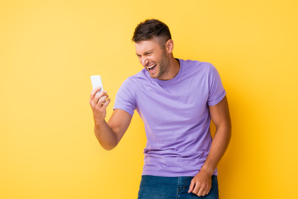 happy man holding smartphone and laughing on yellow  - Foto, imagen