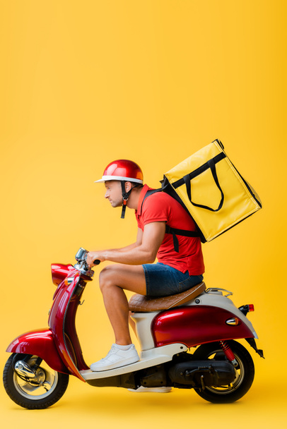 side view of delivery man with backpack riding scooter on yellow - Valokuva, kuva