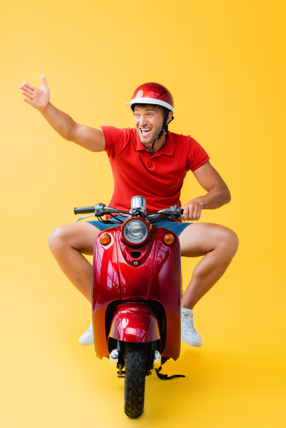 stressed man in helmet riding red scooter and gesturing on yellow - Fotoğraf, Görsel