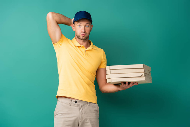 confused delivery man in cap holding pizza boxes on blue - 写真・画像